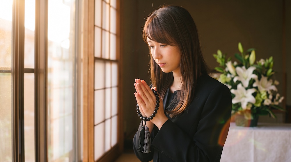 葬儀で手を合わせ祈りを捧げる女性の姿